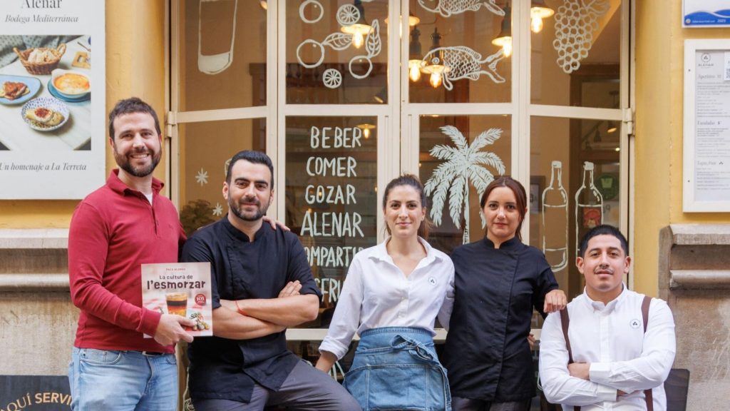 El equipo de Alenar Bodega Mediterránea posa en la puerta del restaurante con el libro 'La cultura de l'esmorzar'.
