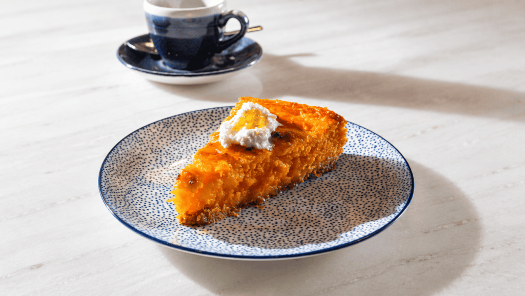 Pumpkin cake with cottage cheese and spicy honey on a blue ceramic plate, with coffee on a marble table at Alenar