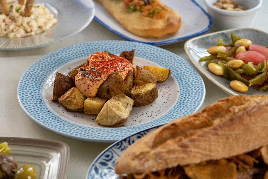 Mesa con tapas mediterráneas en Alenar Bodega Mediterránea Valencia centro — ensaladilla, coca valenciana, patatas y bocadillo para compartir. 